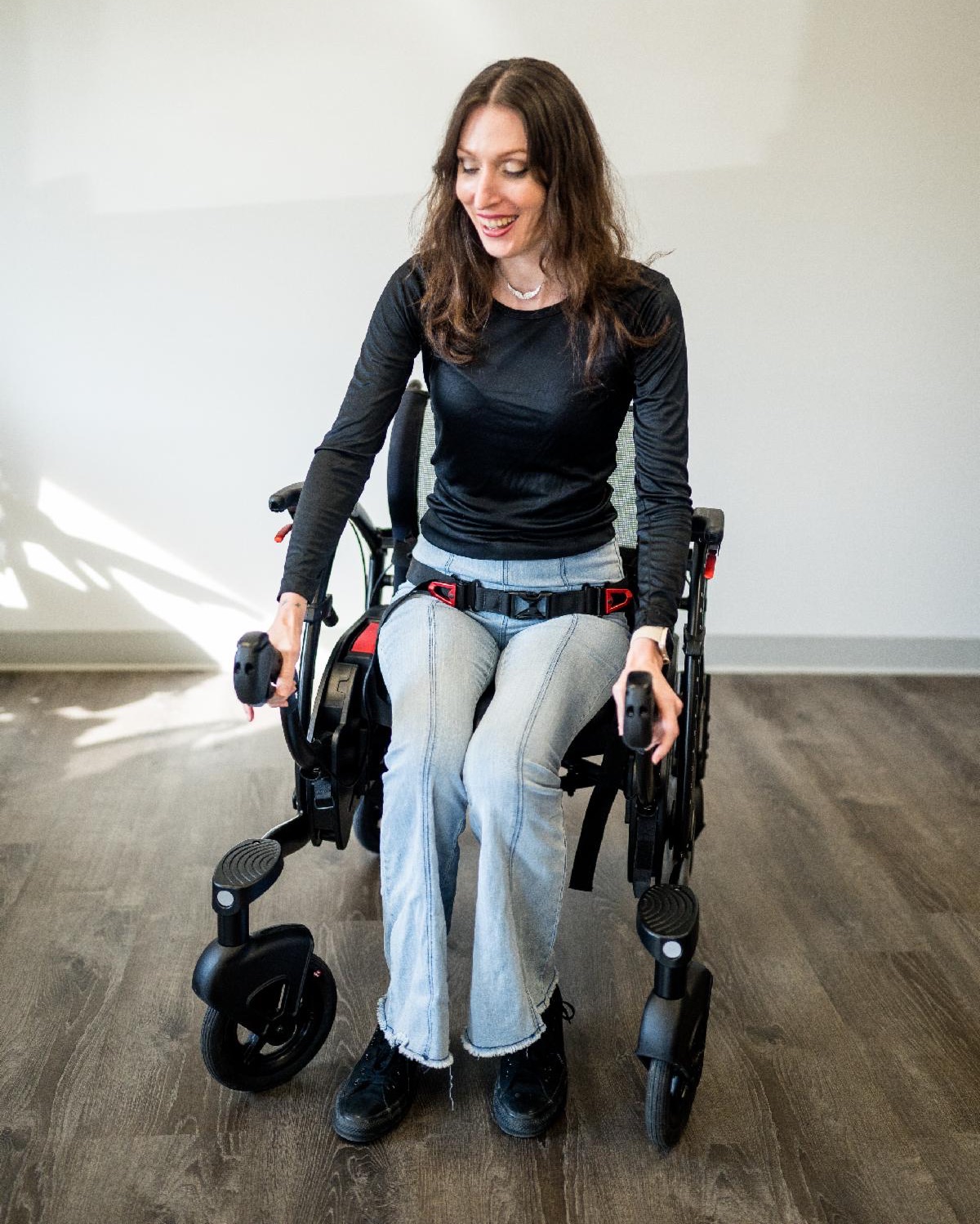 A white woman sits in a Zeen mobility device wearing a black shirt and light blue jeans.