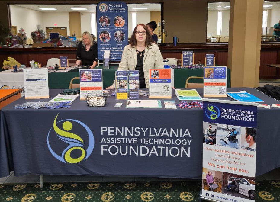 Carmella is wearing a black shirt and tab cardigan. She is standing behind PATF's resource table.