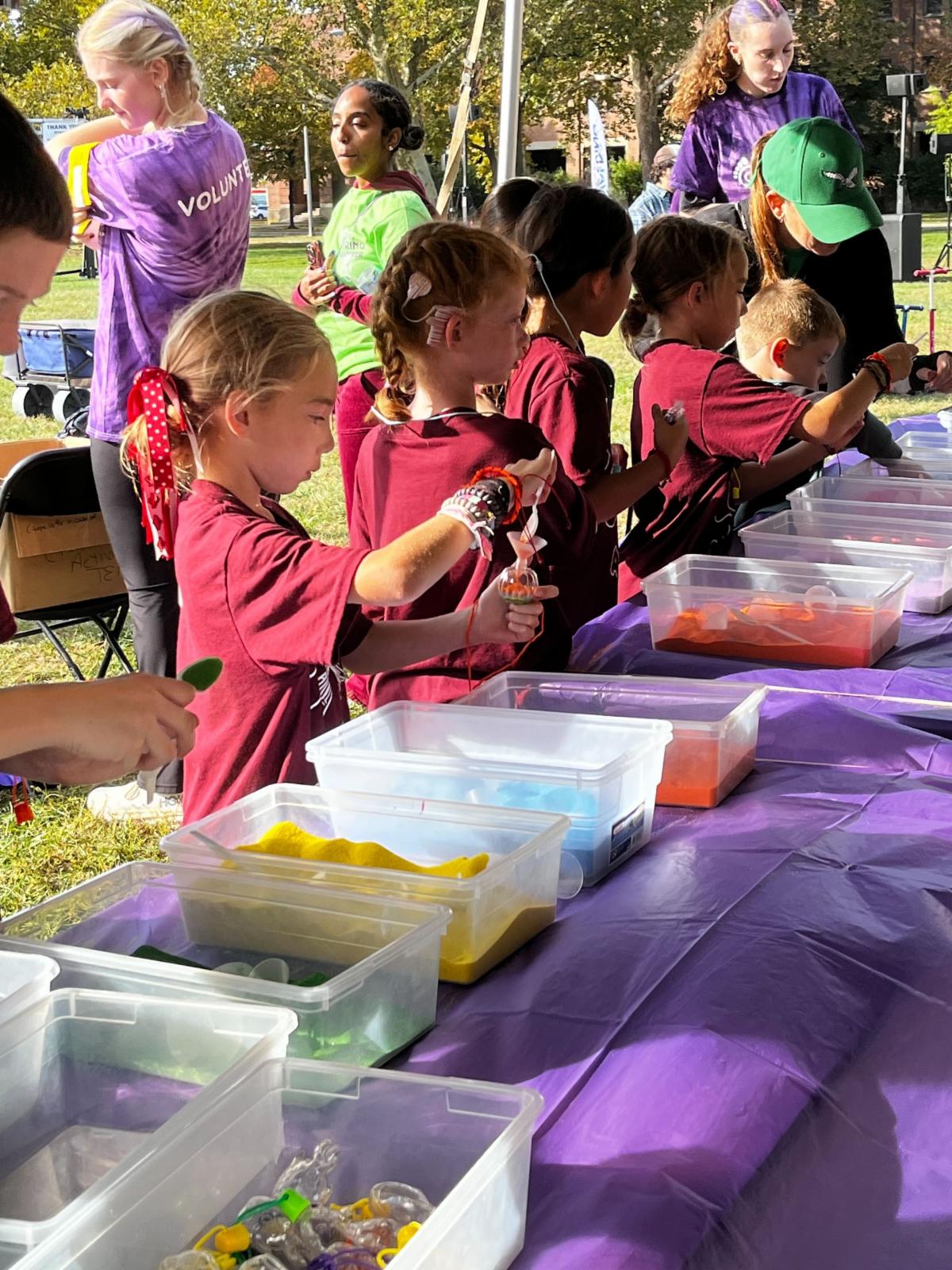 There are children at an activity table playing. They are wearing red shirts.