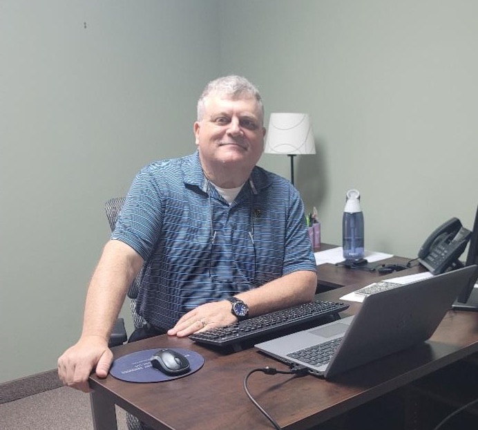 A white man sits at a desk.