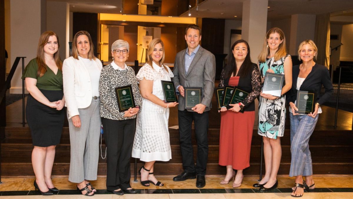 Seven white woman and one white man stand together holding EIFLE Award plaques.