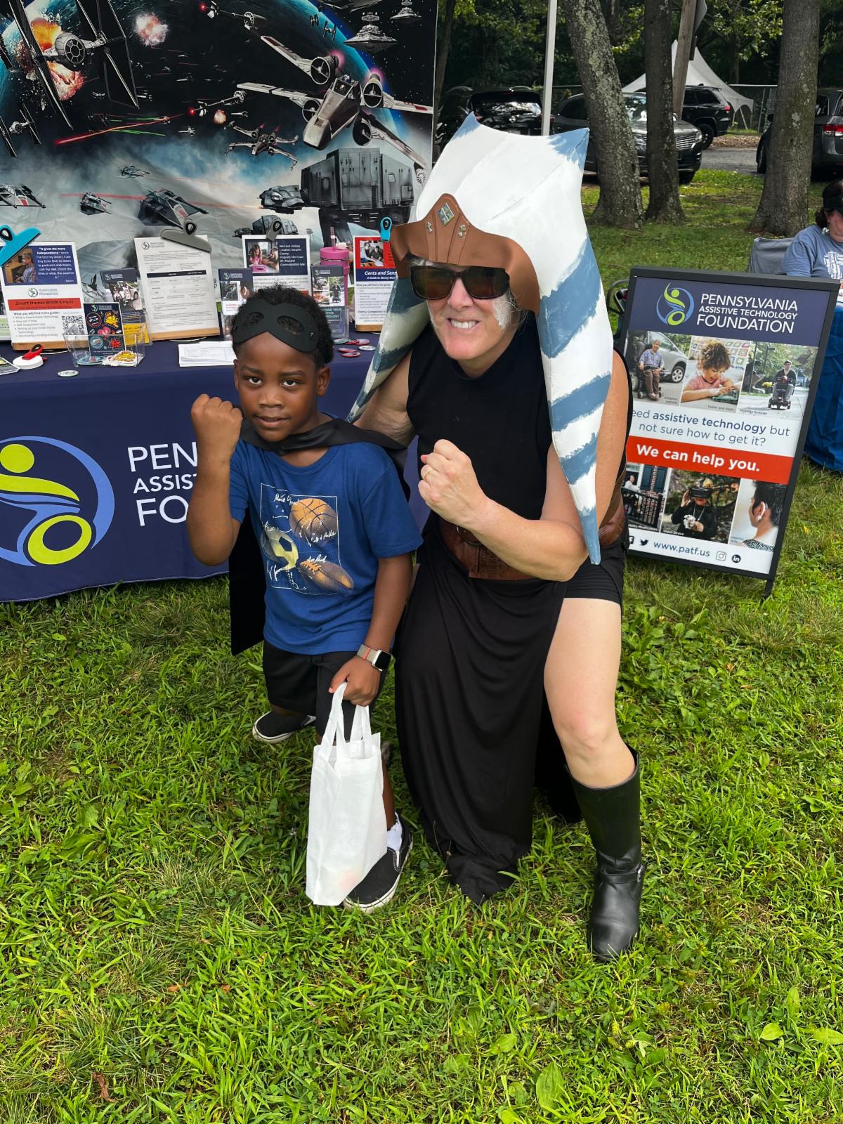 Wendy is dressed up in a Star Wars outfit. She is standing next to a young boy wearing a blue shirt with an eye mask on top of his head and a cape around his neck.