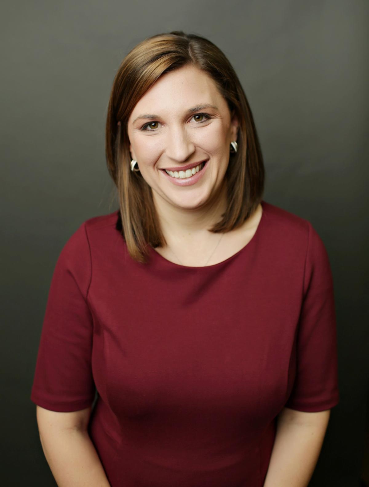 A headshot of Laura. She has brown hair that is straight. She is wearing a maroon shirt.