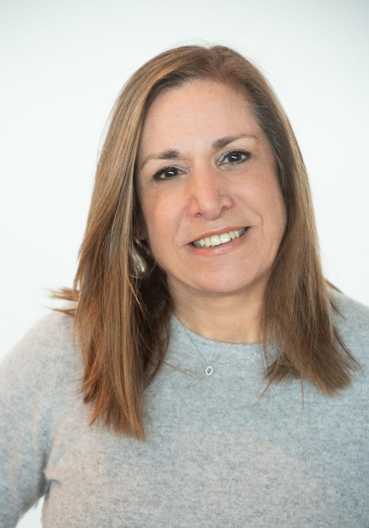 Karen Hassett in light gray sweater, smiling, in front of white background