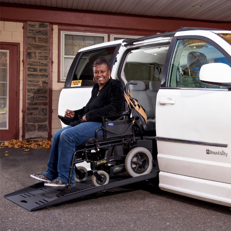 A woman drives her power wheelchair down the ramp of her adapted van.