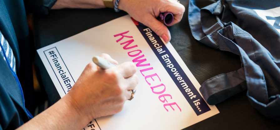 One white hand holds a piece of paper while the other hand writes on it. The paper says Financial Empowerment Is and the person is writing the word Knowledge.