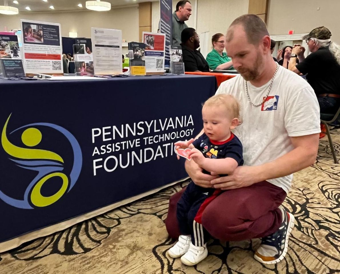 There is a man and his young child kneeling on the ground in front of PATF's resource table.