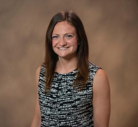Mary Kate is a white woman with brown hair. She is wearing a white and black shirt.