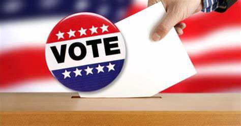 Image of someone dropping a ballot into an election box with the words vote across the front and an American flag in the background