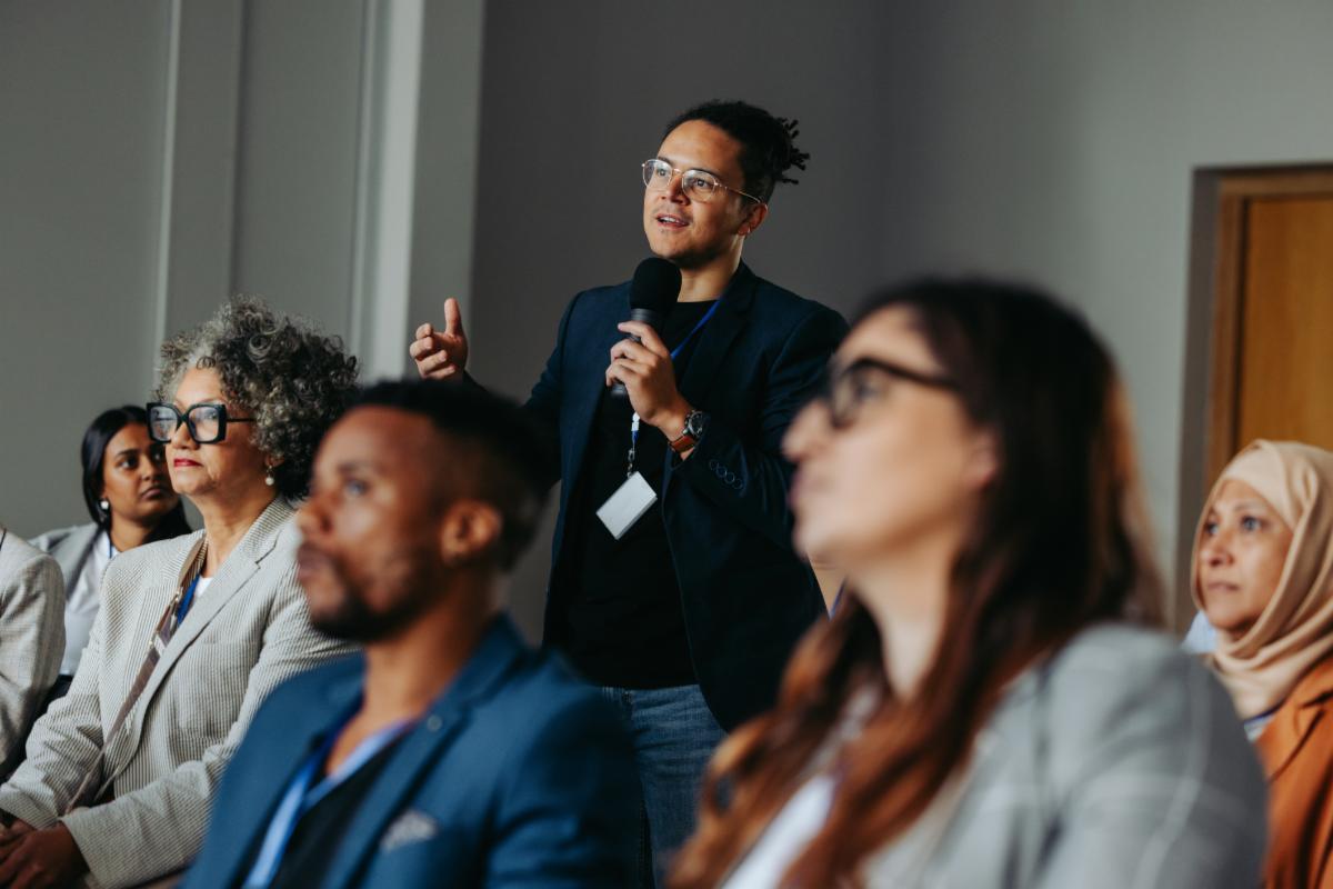 Businessman asking a question during a diverse conference workshop presentation. Attendees are engaged and listening attentively.