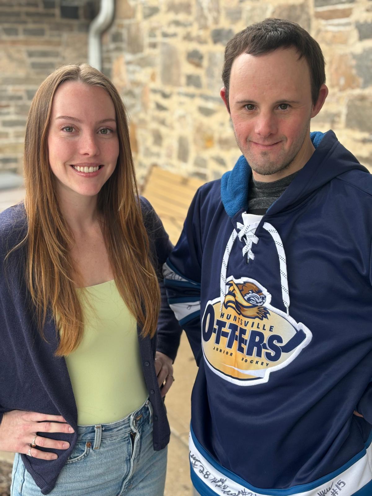 A smiling woman wearing a green top and blue sweater, and a smiling man wearing a blue hockey sweater.