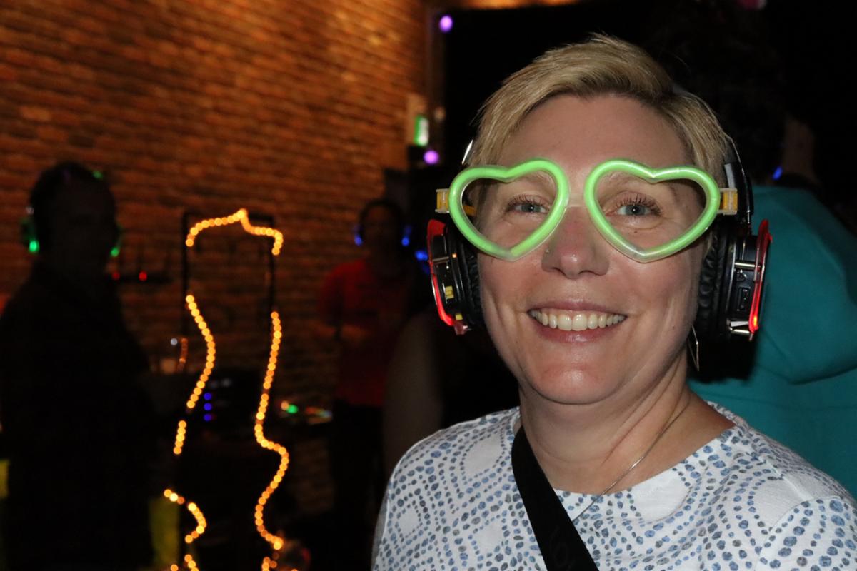 A woman wearing heart-shaped neon green glasses and headphones that glow neon red