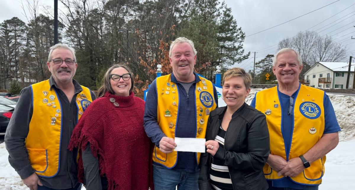 A group of people including 3 in yellow Lions International vests holding a cheque presented to Community Living Huntsville