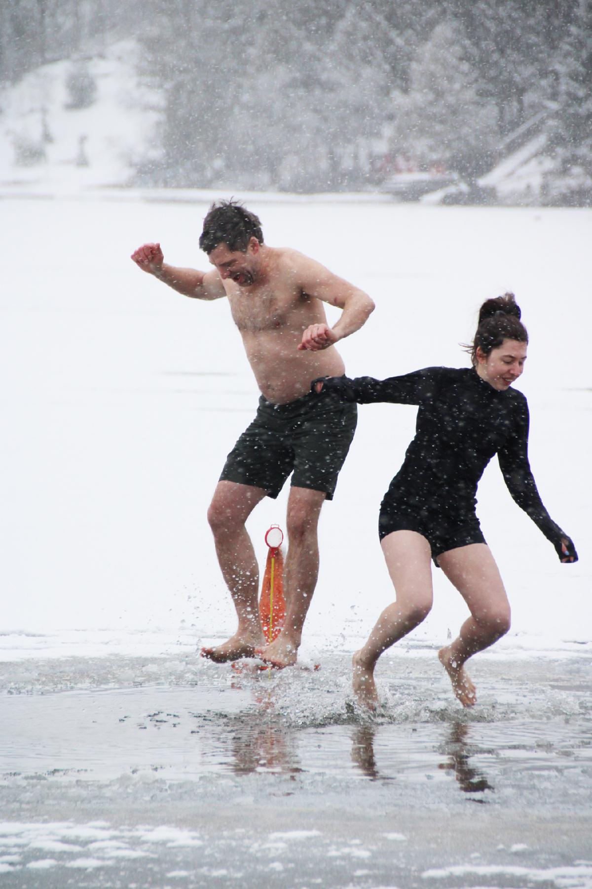 2 people in swimwear smile as they jump into an icy lake in winter