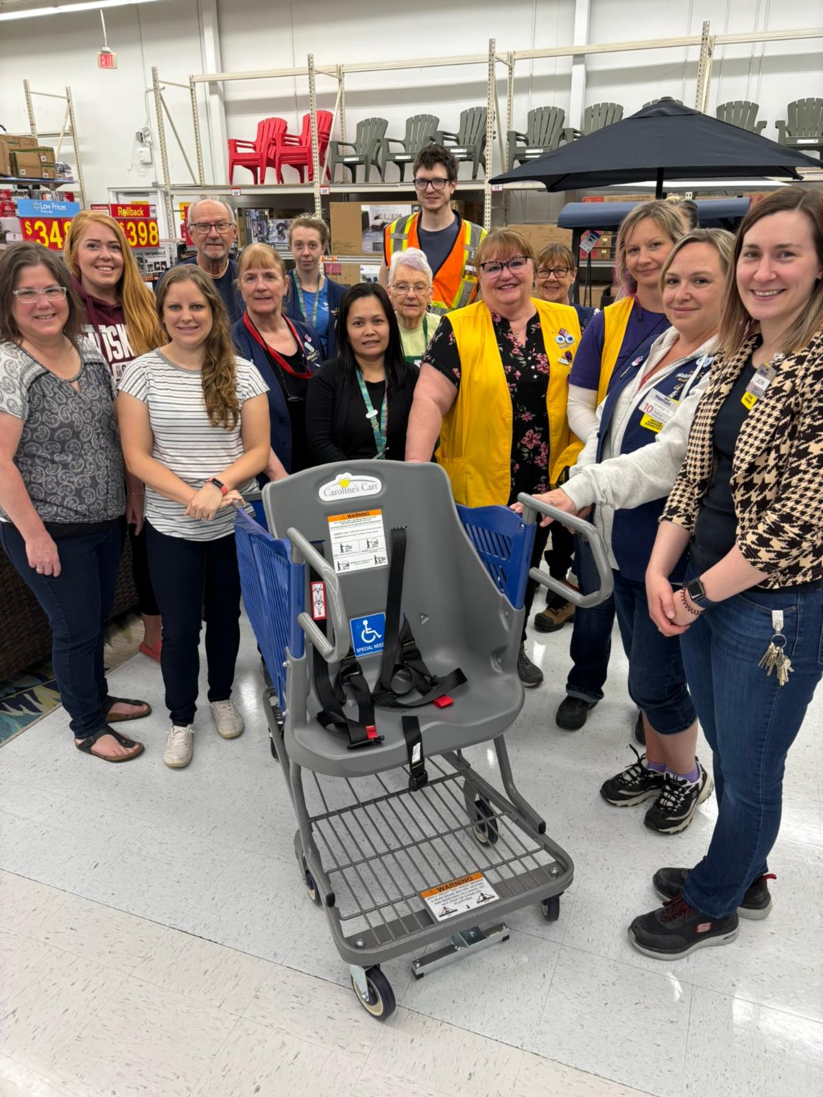 A large group of people standing in a department store surrounding a modified shopping cart with a full sized passenger seat
