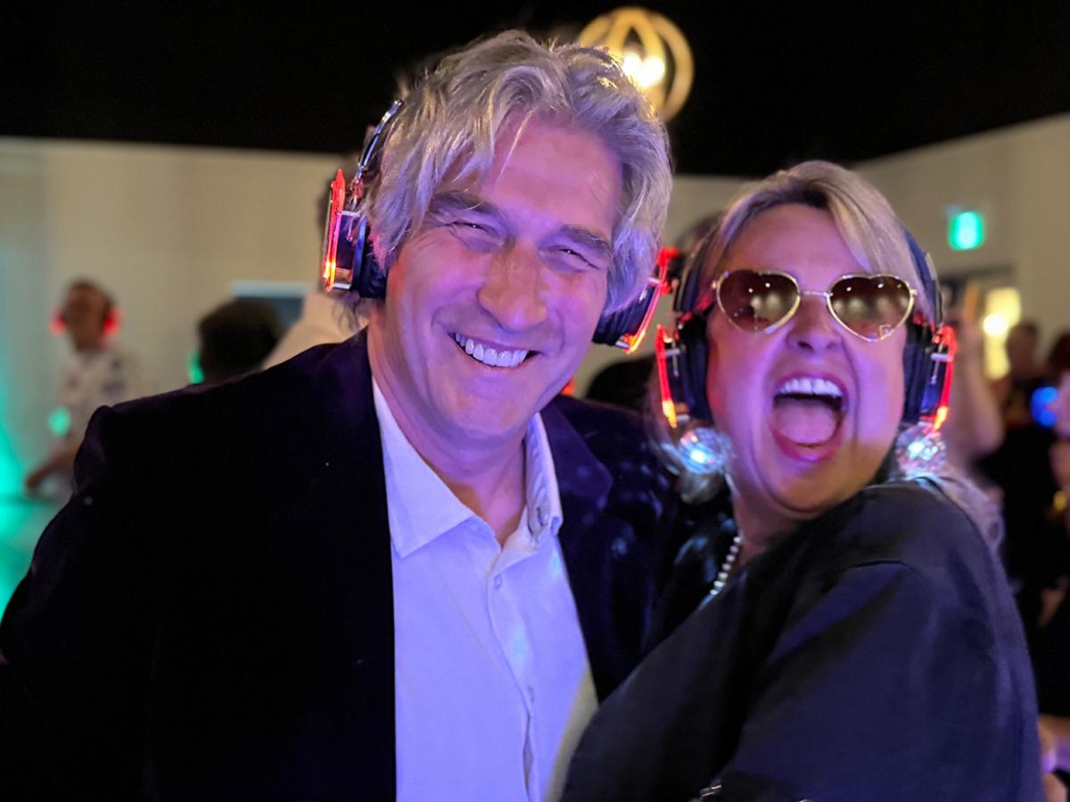 A man and a woman on a busy dancefloor wearing headphones that glow neon red.