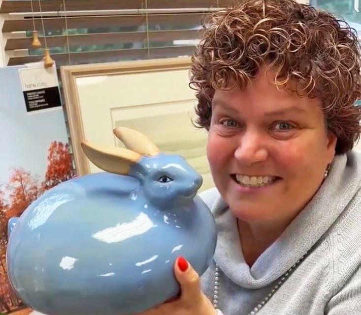 a smiling woman holds a blue ceramic bunny