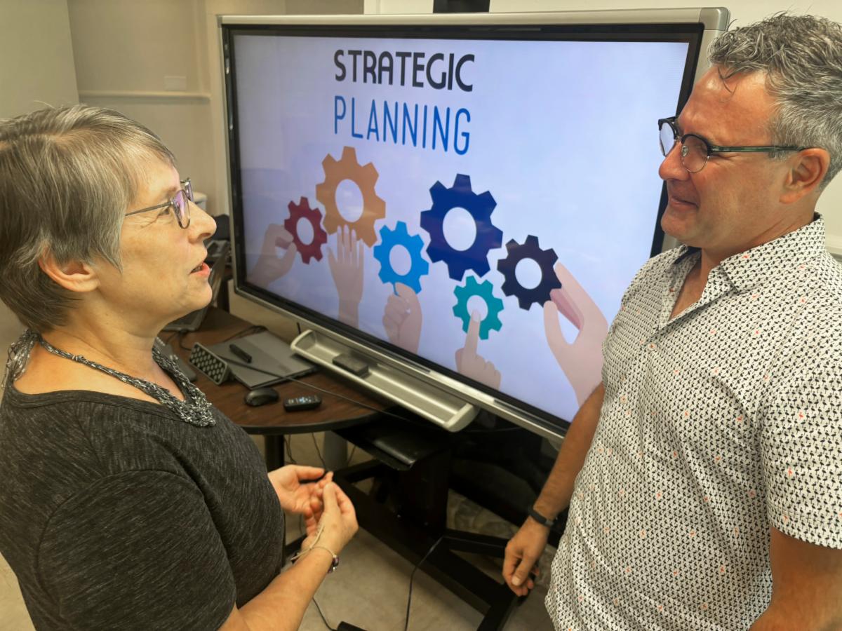 a woman and man talking in front of a display screen that says Strategic Planning