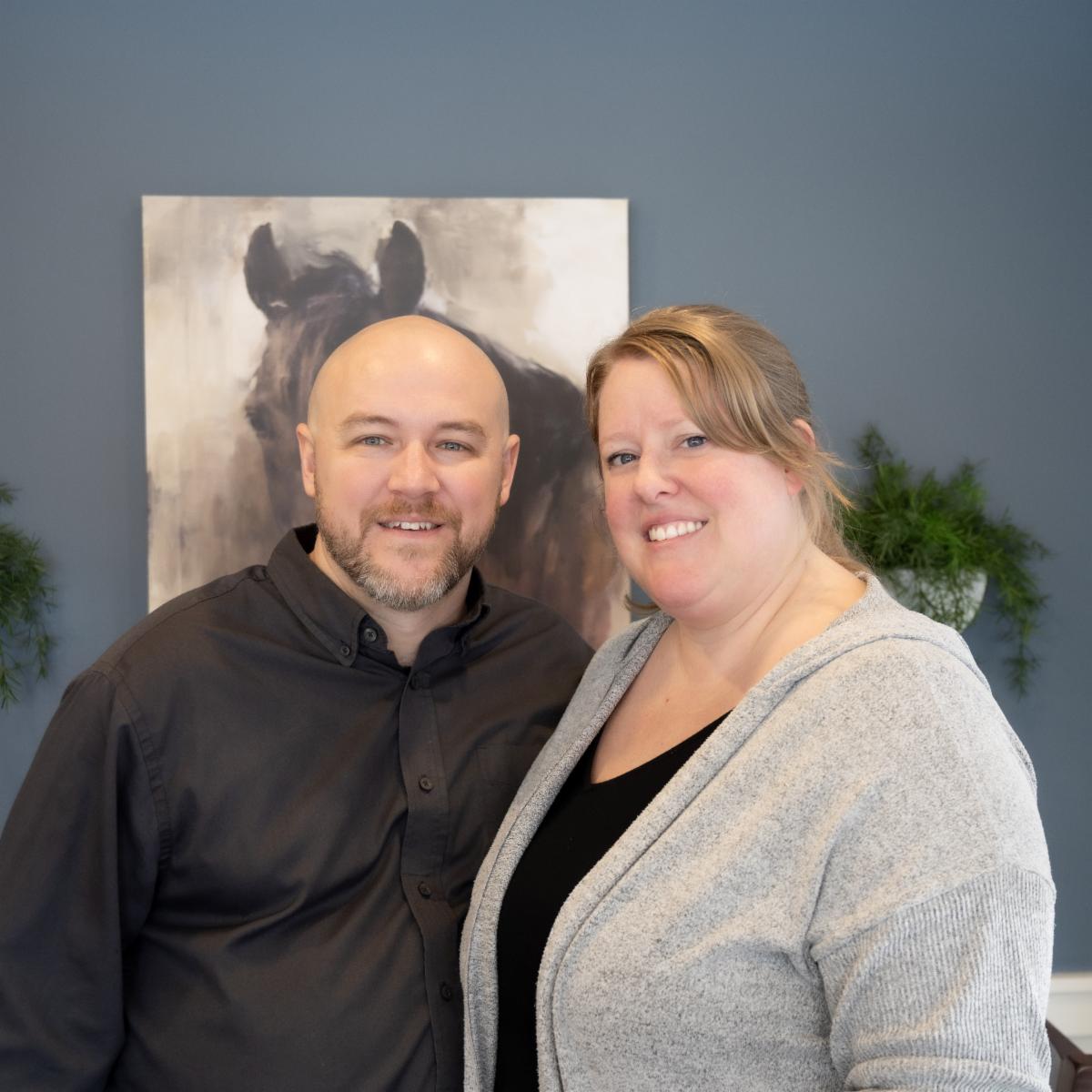 A man Randy and a woman Ashley pose each with 1 arm wrapped around the other