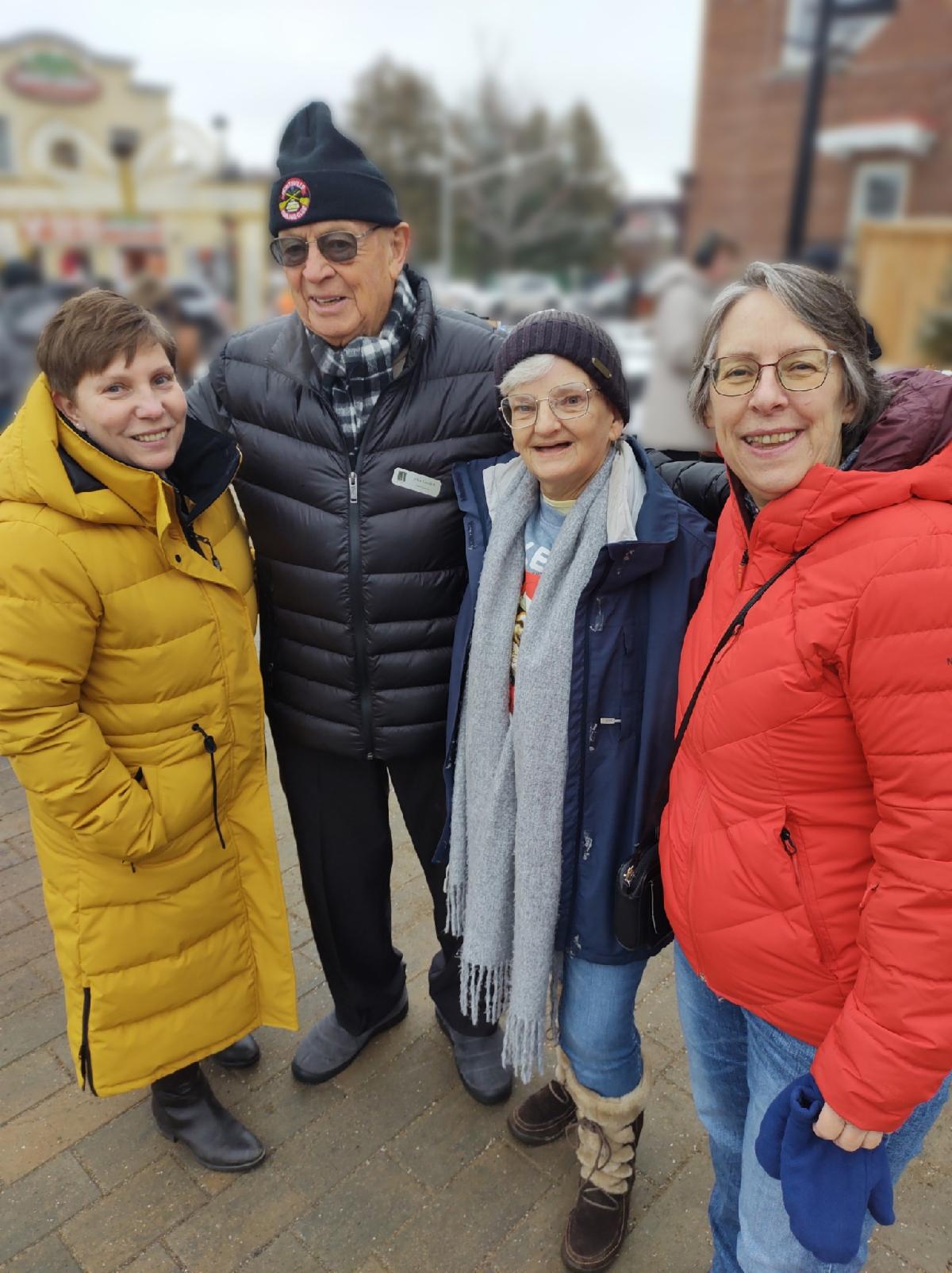 4 people, Suzanne, John, Cindy, and Lorraine, smile while standing outside in winter coats.