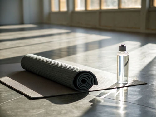 Rolled yoga mat and water bottle on floor with strong sunlight casting shadows_ creating a serene atmosphere in an empty fitness studio space.