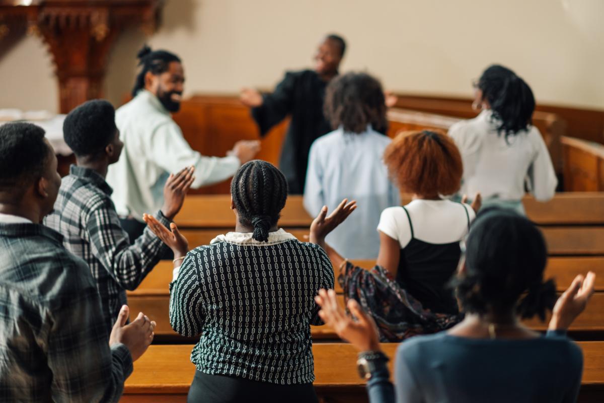 Diverse group of churchgoers are emotionally singing and raising their hands while praying together inside the church