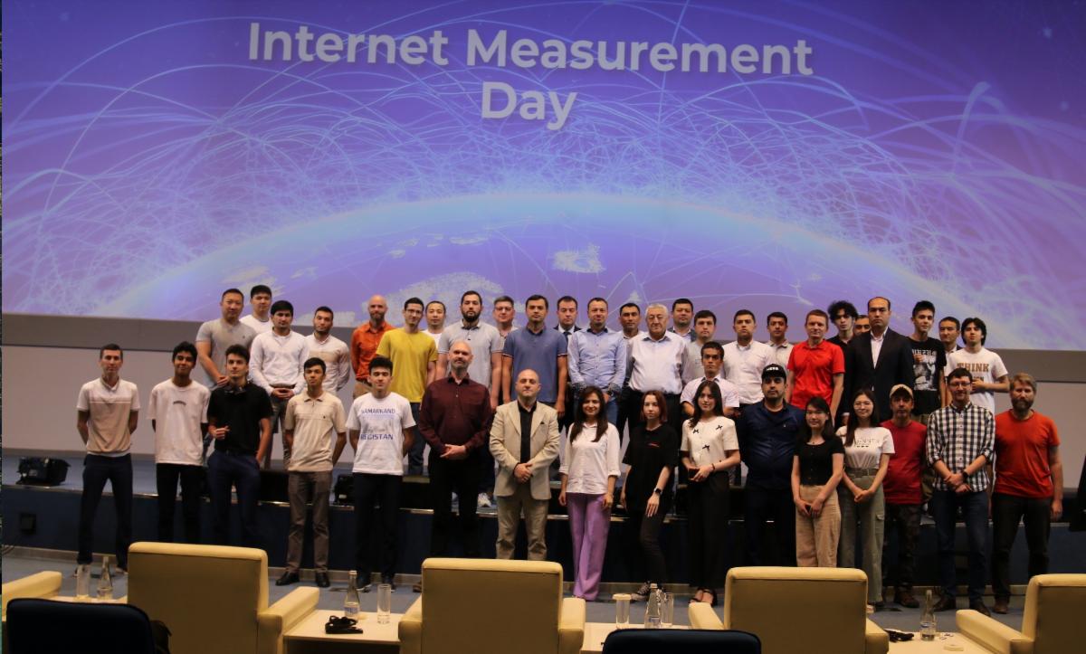 Photo showing the cohort that attended Internet Measurement Day in Uzbekistan. The group is divided into two lines, with both standing in front of a large screen that says “Internet Measurement Day.”