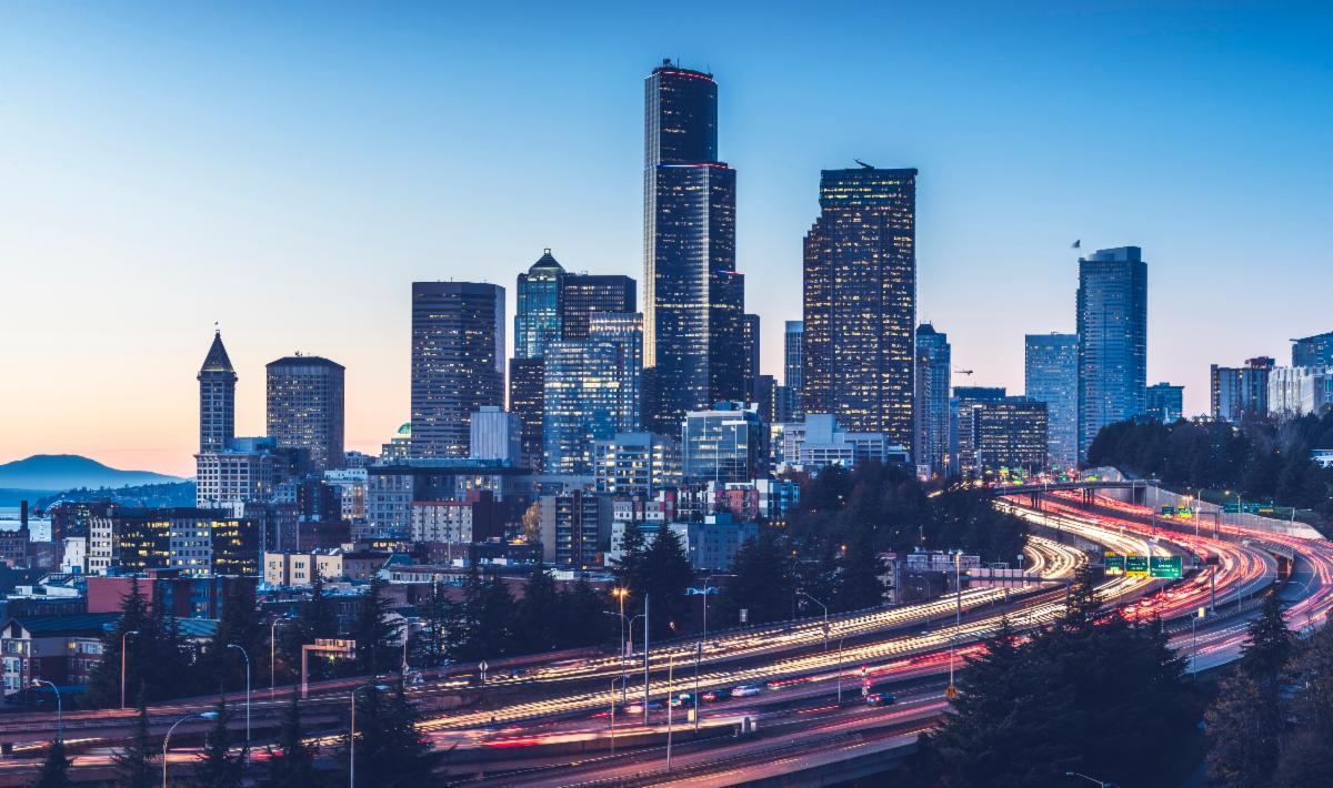 A view of downtown Seattle at night. Cars drive on the highway below, highlighted by their light trails.