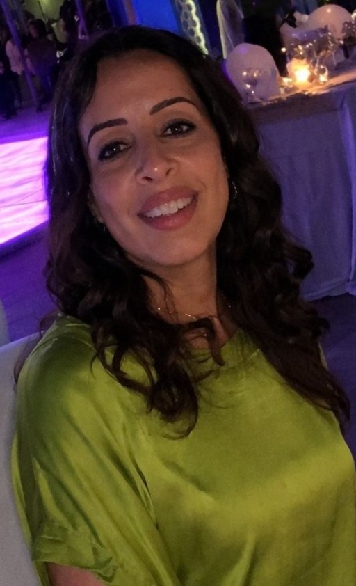ICANN86 Fellowship Program participant Einas Al Shaikh, from Oman. She's wearing a bright green dress in a darkly lit room.