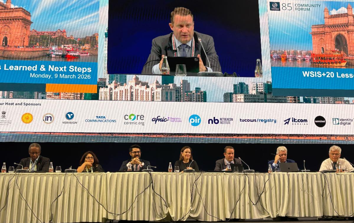 Members of the WSIS+20 “Lessons Learned and Next Steps” session at the ICANN85 Community Forum sit at a long table and speak to the crowd. ICANN President and CEO Kurtis Lindqvist is being broadcasted on the projector screen above.