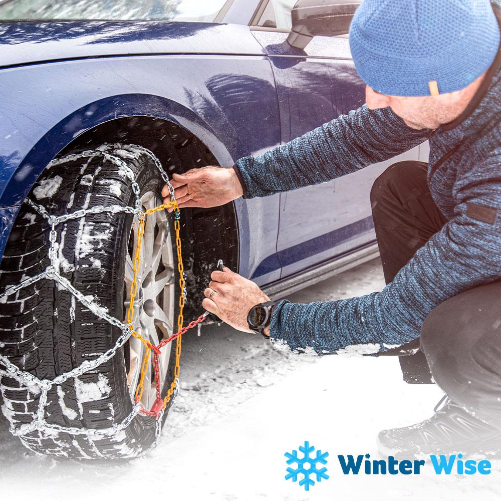A man putting chains on a tire in winter weather. 