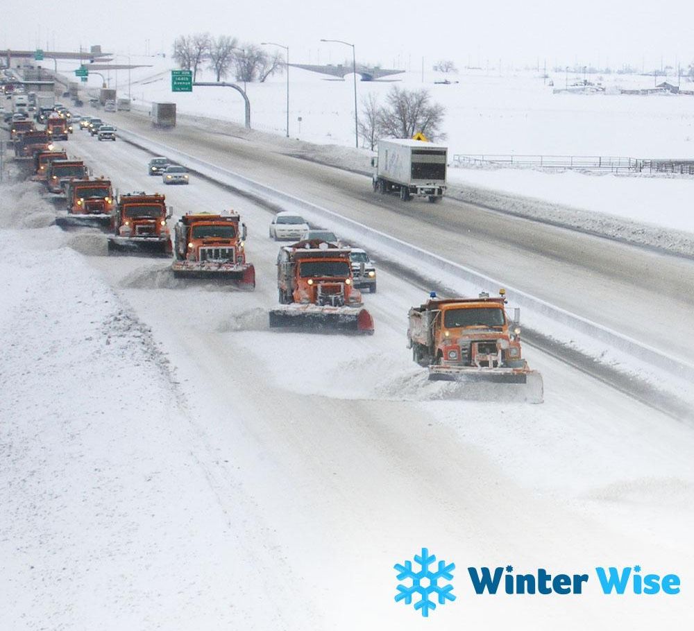 Multiple snow plows driving on a highway in tandem formation. 