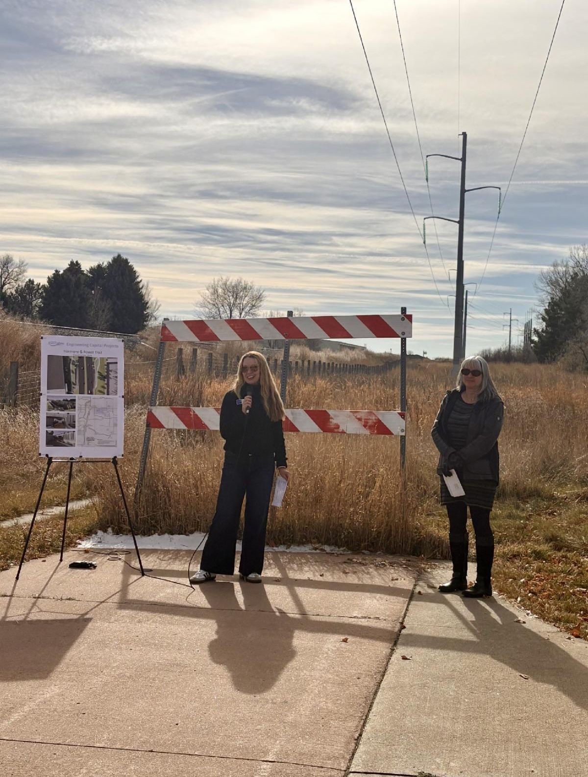A woman speaking at the groundbreaking event next to a project poster. 