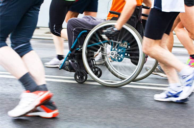 Photo of group of people's legs in a race and a person in a wheelchair running with them