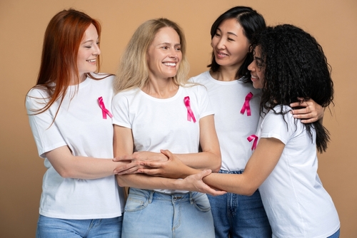 Four diverse women are smiling and showing their support for a friend battling breast cancer standing isolated on beige background. Support_ health care concept