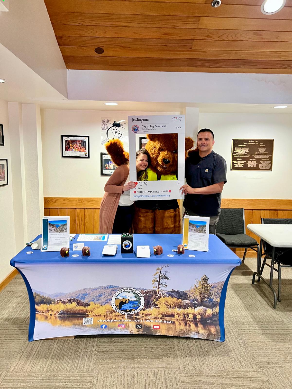 Rachel Bowman and Javier Navarrete posing for a photo with Grizzwold The Bear atthe City's booth at the 2025 Job Fair and Resource Event