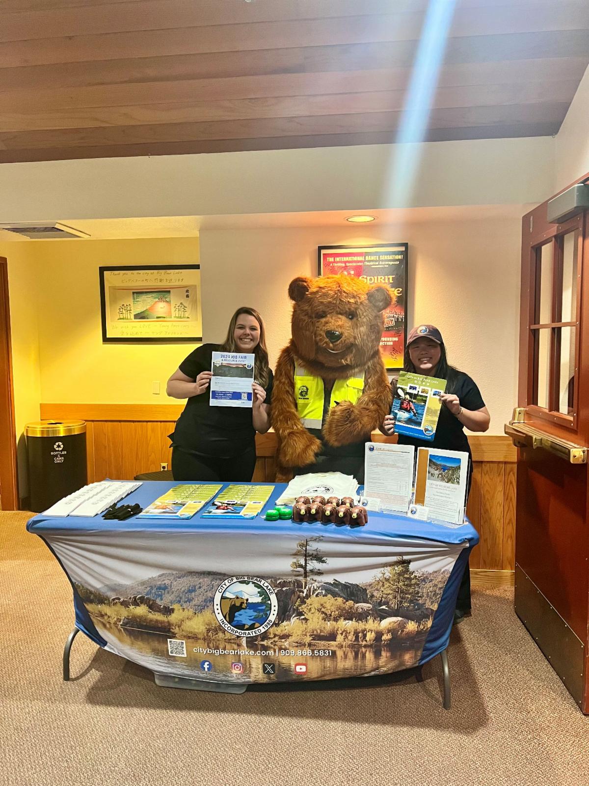 City staff and City mascot Grizzwold The Bear holding brochures at the City's job fair booth