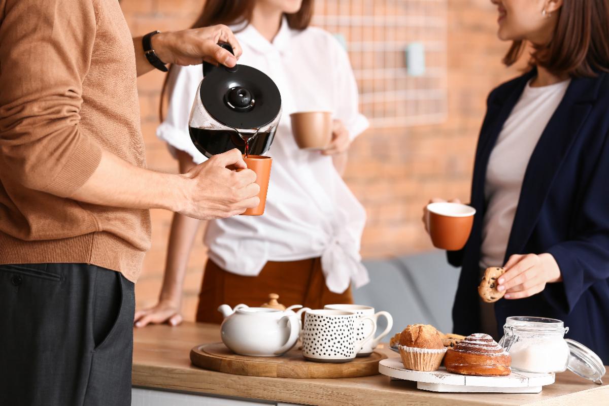 3 standing adults chatting over coffee and pastries