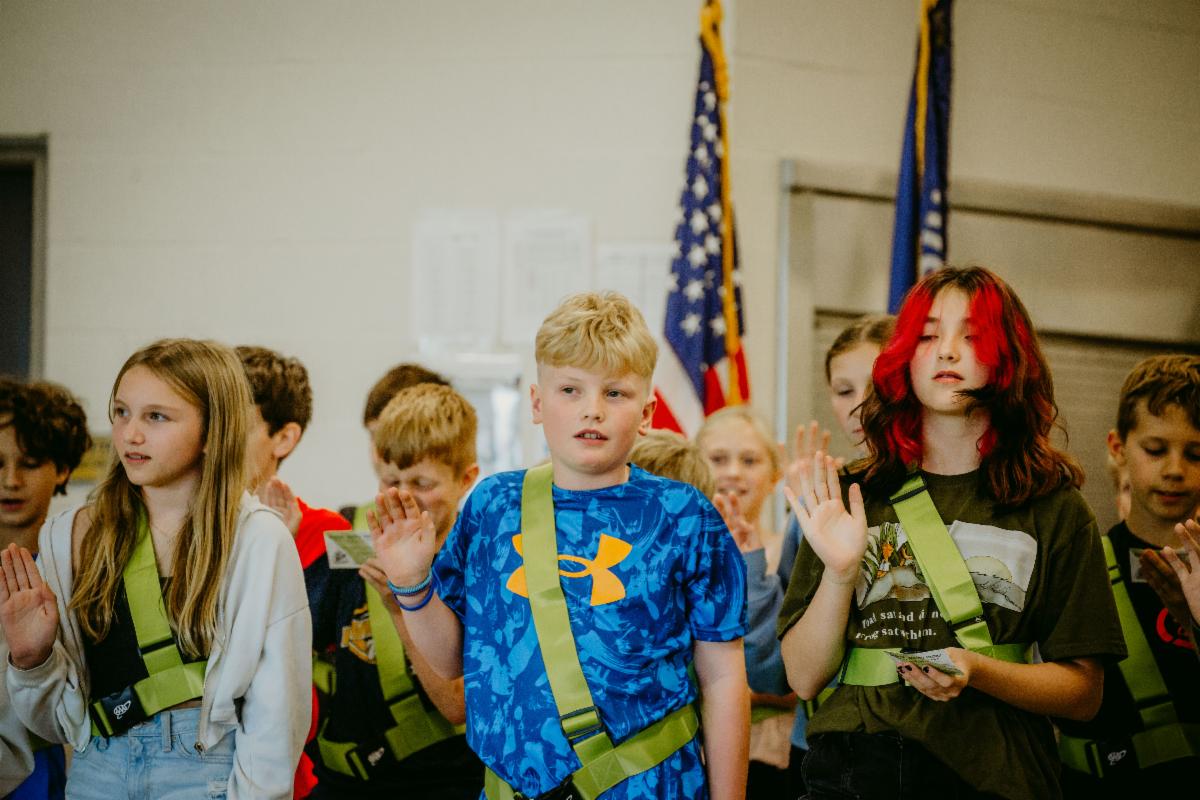 two girls and a boy hold up an arm and take an oath