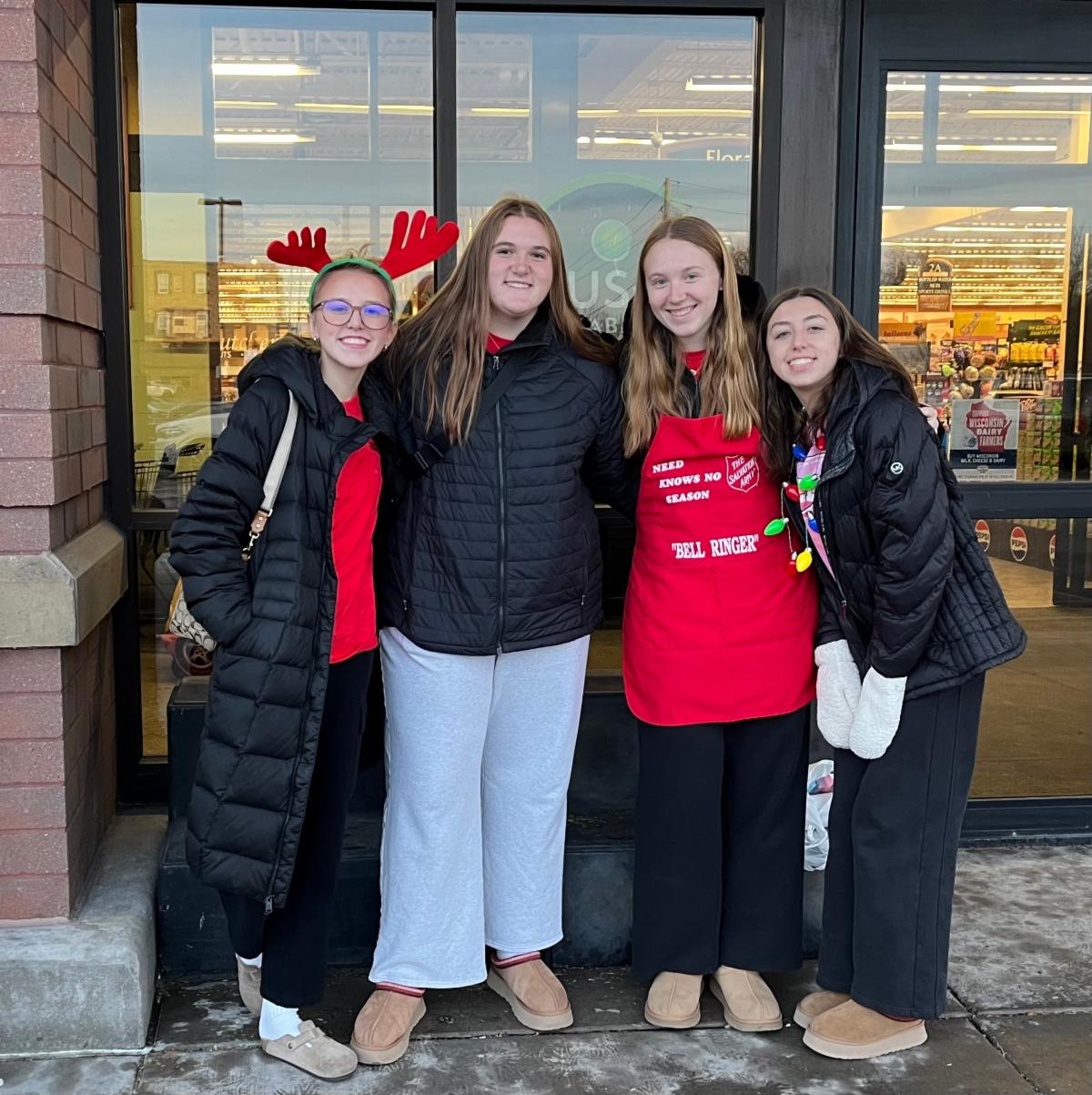four student pose while ringing bell at grocery store entrance