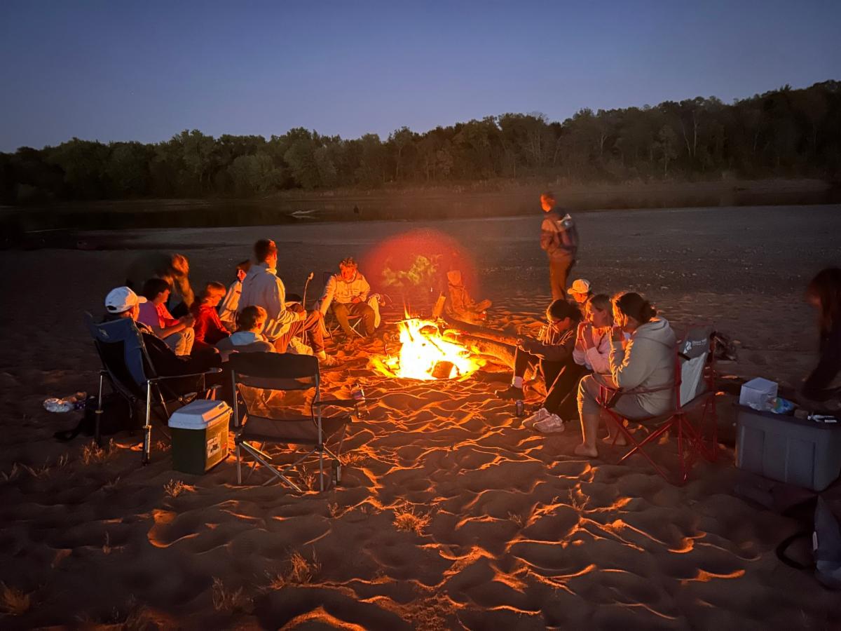 boys and girls sitting around a fire with tents on a beach