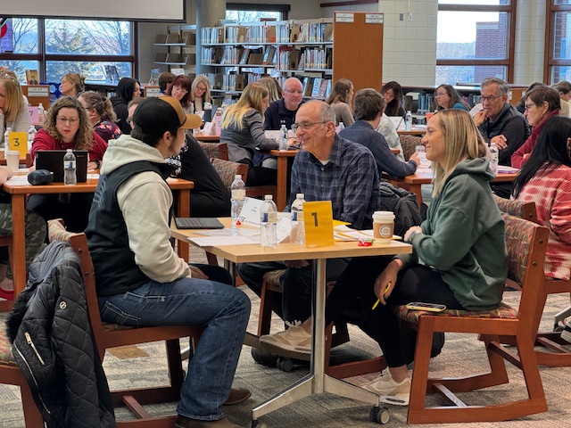two adults speaking with a student at at table