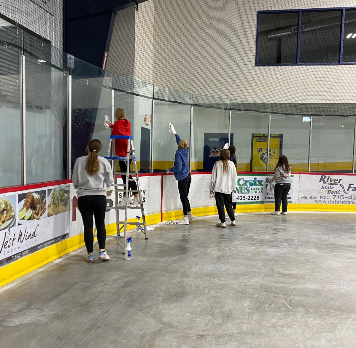 students cleaning the glass at a hockey rink