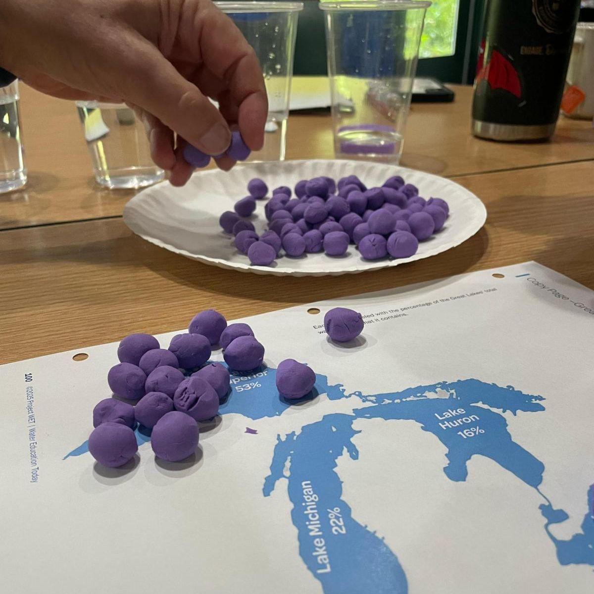 Educator placing balls of playdough on a Great Lake basin map to model lake volume.