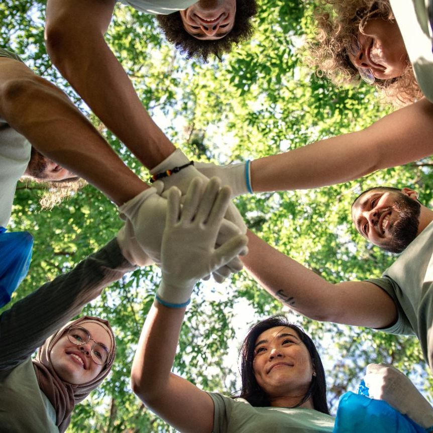 Group of happy adults in a circle with their hands stacked on top of each others in a group huddle.. 