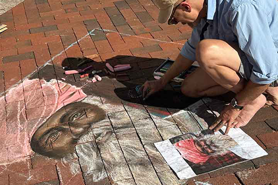 An artist drawing a chalk portrait on the ground during Chalkfest