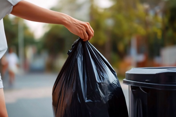 Person taking a trash bag to the can on the curb