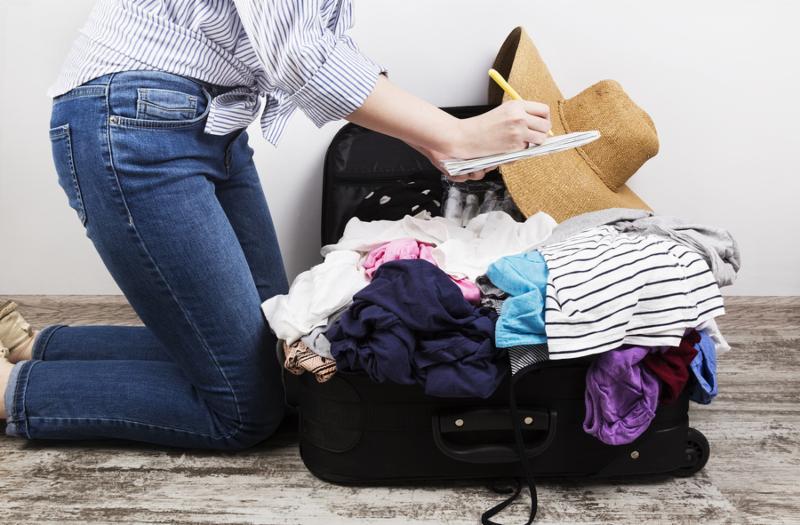 Young girl casually packs black suitcase. Packing list in white notebook