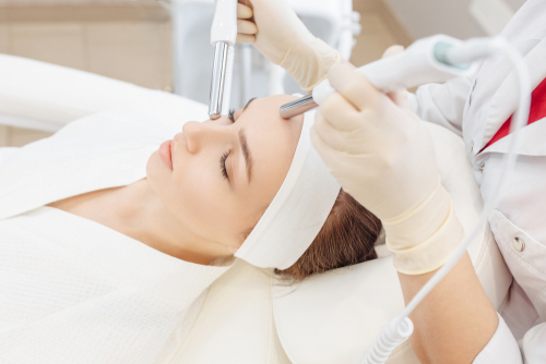 Beautician makes a microcurrent massage of the face of the girl client with the help of modern salon equipment. The concept of hardware cosmetology