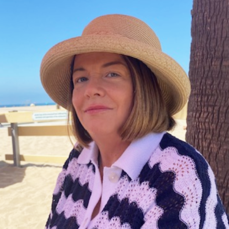 Cherie Garrity headshot shows her in a striped shirt and tan hat in front of a beach